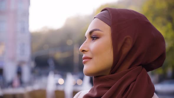 A Young Beautiful Muslim Woman Looks Around with a Smile in a Street in an Urban Area