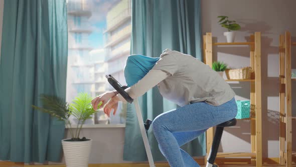 Tired Muslim Woman in a National Headscarf is Working Out on an Exercise Bike in Her Living Room