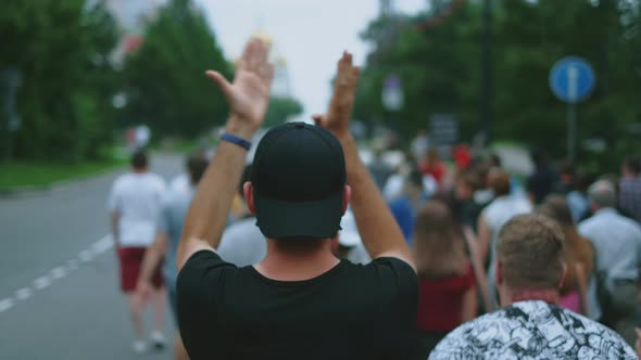 Peaceful protester claps hands while marching with oppositional people in crowd