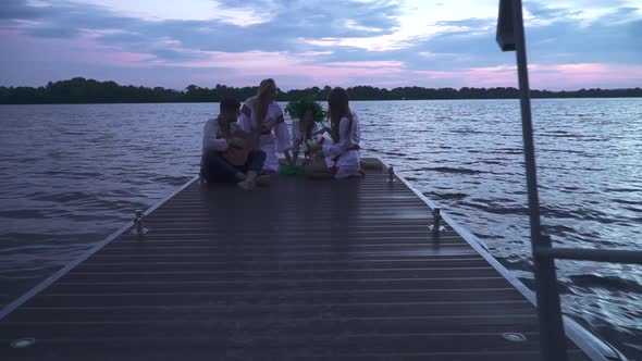 Three Girls and a Guy with a Guitar Are Sitting on the Pier
