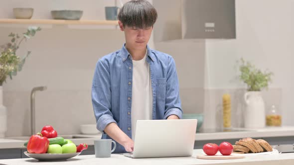 Young Asian Man Working on Laptop in Kitchen