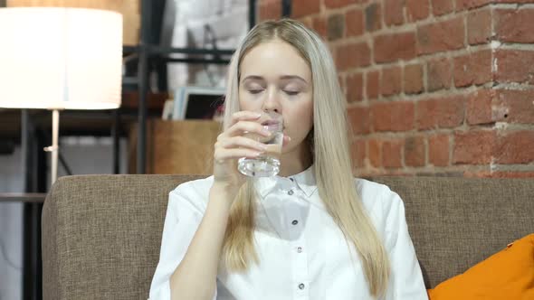 Woman Drinking Water in Glass, Sitting on Sofa