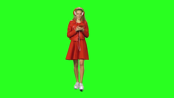 Blonde Girl Is Walking in Big Red Headphones, Chooses Music and Moves To Rhythm at Green Screen