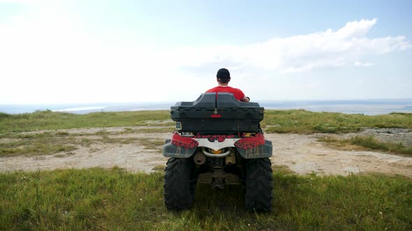 Man in a Black Cap and Red T-shirt on a Colored ATV Rides