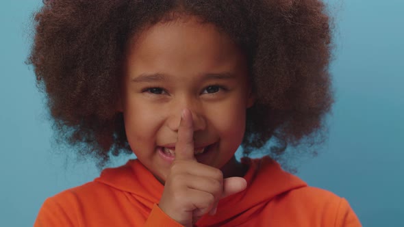 cute African American girl making silence gesture with forefinger by mouth