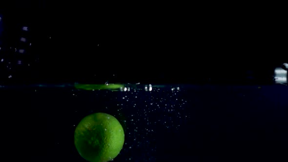 Super slow motion shot in reverse of whole lime falling into water and coming out of it