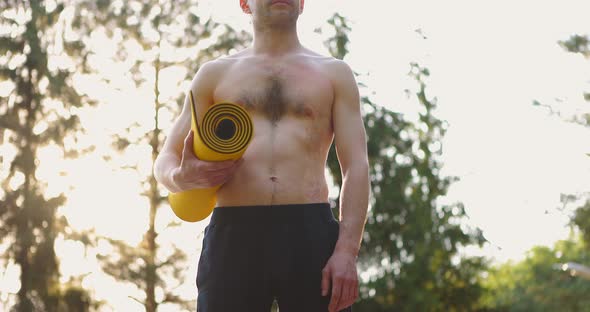 Tilt Shot of Young Man with Sport Mat in Hands Standing and Looking Forward