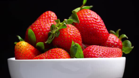 Appetizing strawberries with wilted green leaves lie on white porcelain bowl