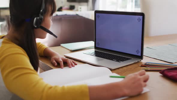 Asian girl at home wearing headset during online school lesson using laptop, copy space on screen