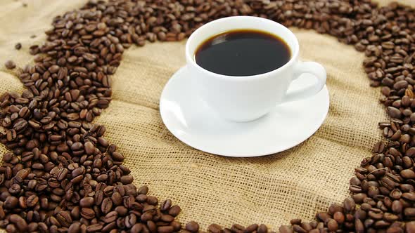Cup of coffee surrounded with roasted beans
