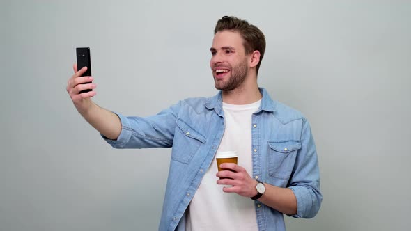 Bearded young caucasian man wearing jeans shirt talking on mobile phone and holding cup of coffee