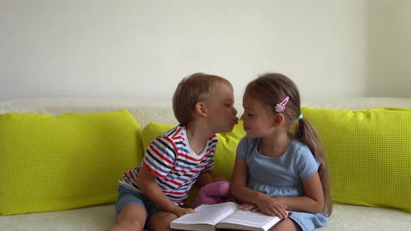 Two Smiling Preschool Toddler Children Read Interesting Book of Fairy Tale On Couch