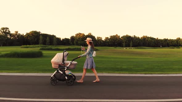 Happy Woman Walking with a Pram in the Park