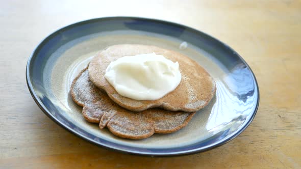 Spreading white vanilla yogurt onto a stack of whole wheat pancakes for a healthy breakfast.