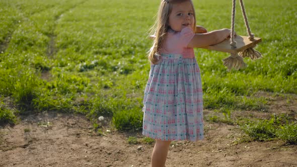 Little 3 Year Old Girl Trying to Climb a Rope Wooden Swing