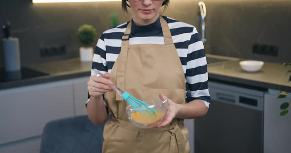 Housewife in Glasses Standing in front of Camera While Mixing Eggs with Whisk