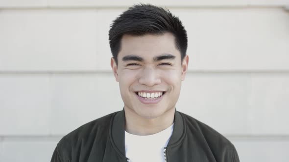 Young Asian Man Smiling Confidently at Camera While Standing on City Street