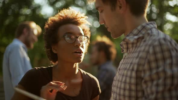 Beautiful Darkskinned Female Talking Smiling with Caucasian Male with Tablet in Park in Slowmotion