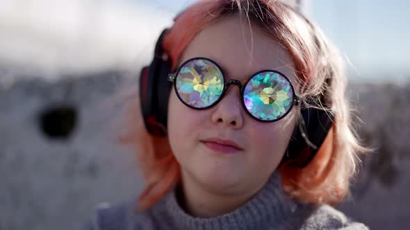 Preteen Girl is Enjoying Music By Headphones on Street Portrait of Child with Funny Glasses