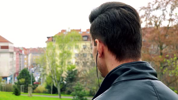 Young Man Stands and Listen To Music From Earphone in Park - Detail From Behind