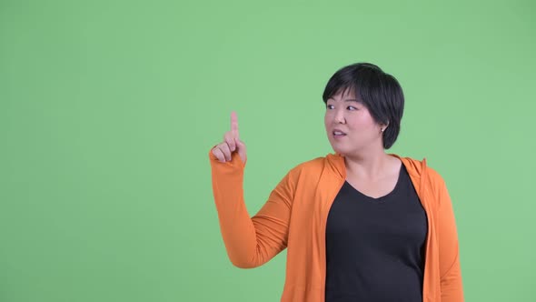 Happy Young Overweight Asian Woman Talking and Pointing Up Ready for Gym