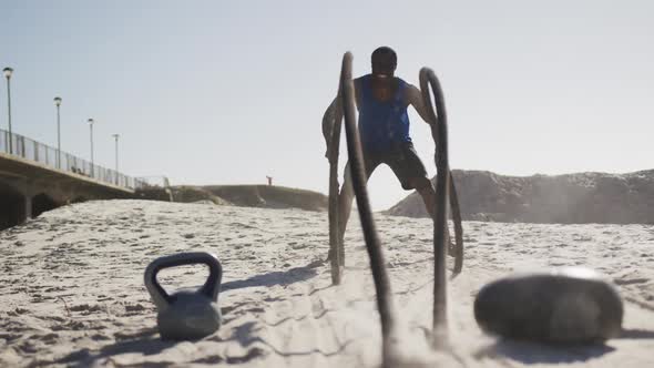 Focused african american man exercising with battling ropes outdoors on beach