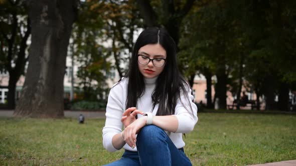 Caucasian Woman Sitting on Grass and Looking at Smartwatch