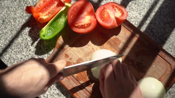 Slicing White Onion On Cutting Board With Tomatoes And Bell Pepper On The Side. - high angle