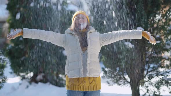 Joyful Young Slim Woman Tossing Snow on Sunny Winter Day Outdoors Posing in Park Forest