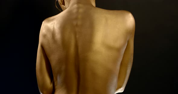 Bare Lady Back with Golden Colour Skin Poses Against Black