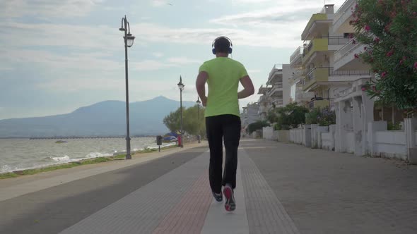 Young Man in Headphones Runs on Road of City Perea, Greece