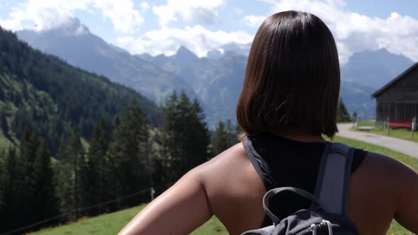 Rear view of female hiker getting ready for her tour through the mountains, puts on backpack and sta