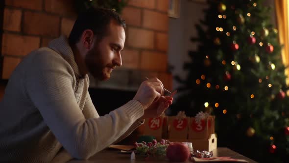 Side View of Relaxed Young Man Writing Number on Red Bag By Brush and White Paint Sitting at Table