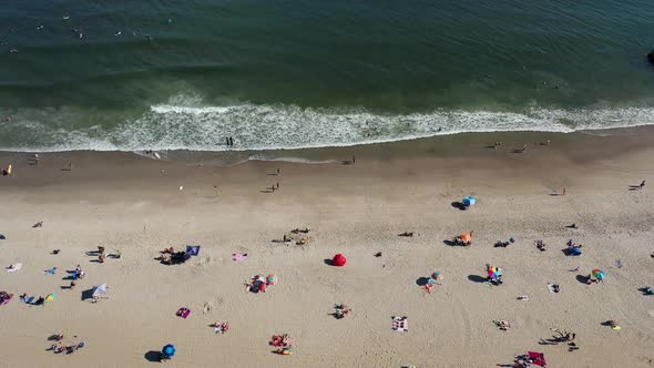 A bird's eye view over people relaxing on the beach on a sunny day. The drone camera truck right whi