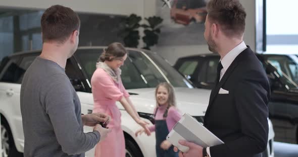 Happy Caucasian Little Girl Running From Background To Father Buying New Automobile and Taking Car