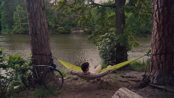 A Man Traveling By Bicycle Resting in a Green Hammock and Enjoying the Scenery Relaxing in Woods By