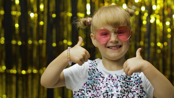 Child Show Thumbs Up, Smiling, Looking at Camera. Girl Posing on Background with Foil Golden Curtain