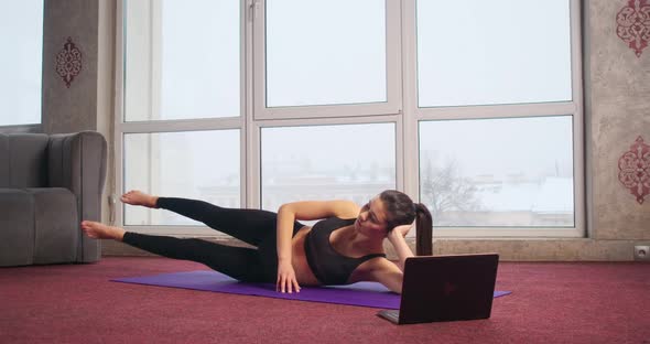 Slim Flexible Brunette Girl Lying on Back on Yoga Mat Raising Legs Meditating