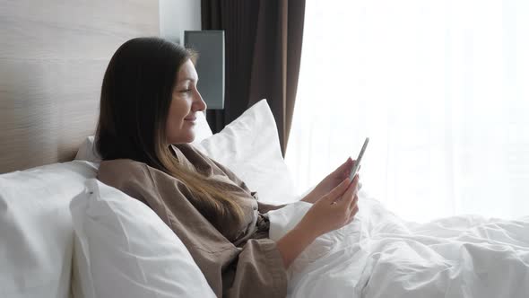 Girl in Bathrobe Studies Online with Tablet in Hotel Bed