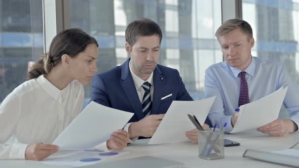 Middle Aged Businessman Discussion Documents with His Assistants on Office Table