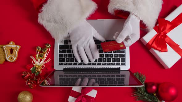 Top View Santa Hands in White Gloves are Typing on the Keyboard By Red New Year Decorated Table