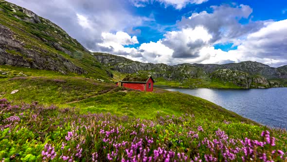 Red cabin between lake and mountain, heather and cloudement, Norwegian countryside; time-lapse