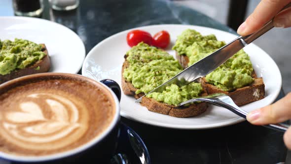 Female Hands Cutting Avocado Toast While Having Breakfast With Coffee