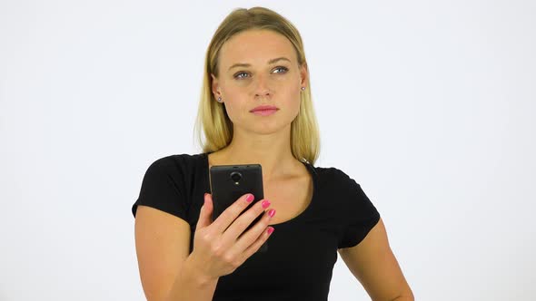 A Young Beautiful Woman Looks at a Smartphone with a Smile - White Screen Studio