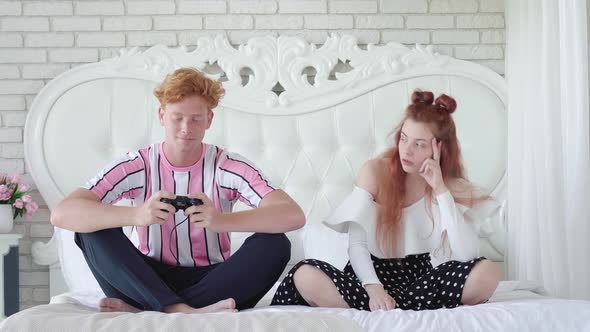 Irritated Woman Looking at Redhead Man Playing Video Games. Portrait of Young Caucasian Couple