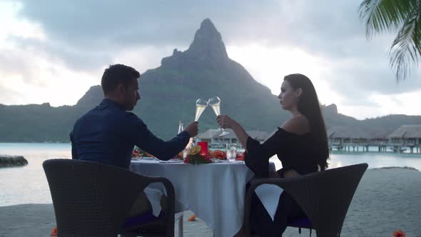 Man and woman couple toasting with champagne on beach, tropical island resort sunset, Bora Bora
