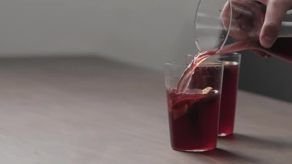 Slow Motion Man Hand Pour Mulled Wine in Thin Tumbler Glasses on Walnut Table