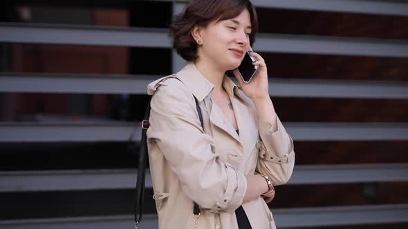 Cute Woman Chatting in Smartphone in Trench Coat