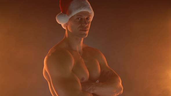 Portrait of Muscular Man Wearing Christmas Santa Hat Folded Hands on Smoky Background