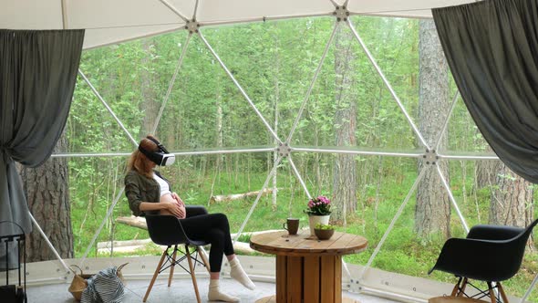 pregnant woman wearing virtual reality glasses in a tent overlooking the forest